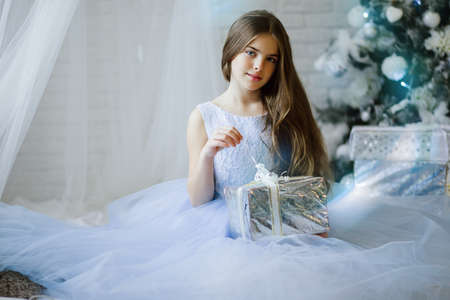 Beautiful girl is sitting near christmas tree with silver gift boxの写真素材