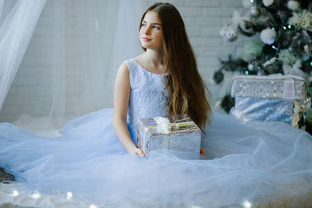 Beautiful girl is sitting near christmas tree with silver gift boxの写真素材