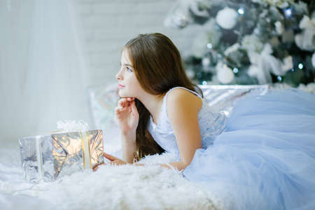 Cute girl is sitting near christmas tree with silver gift boxの写真素材