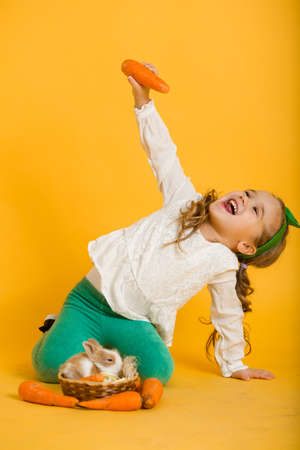 Pretty happy child girl with carrots and her friend little colorful rabbit, Easter holiday conceptの写真素材