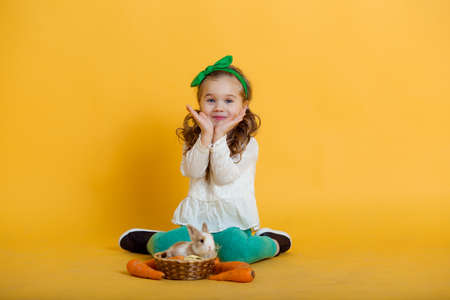 Pretty happy child girl with carrots and her friend little colorful rabbit, Easter holiday conceptの写真素材