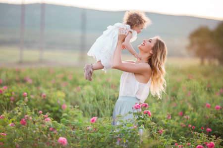 Beautiful child girl with pretty young mother are wearing casual clothes are walking in spring garden with pink blossom rosesの写真素材