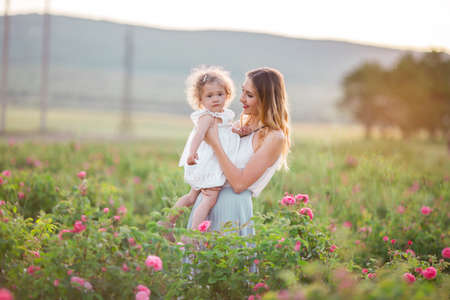 Beautiful child girl with pretty young mother are wearing casual clothes are walking in spring garden with pink blossom rosesの写真素材