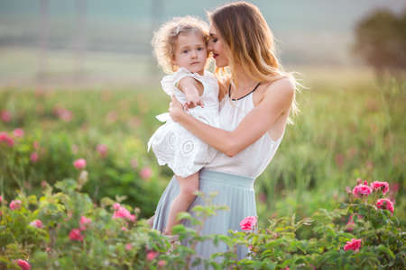 Beautiful child girl with pretty young mother are walking in spring garden with pink blossom roses flowersの写真素材