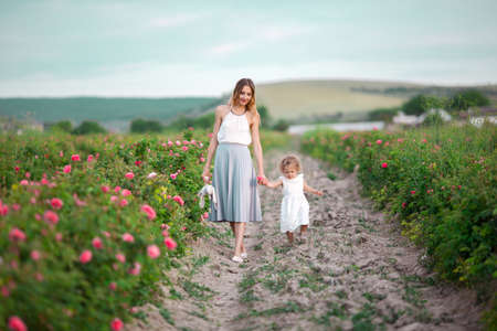 Beautiful couple child girl with pretty young mother are walking in spring garden with pink blossom roses flowersの写真素材