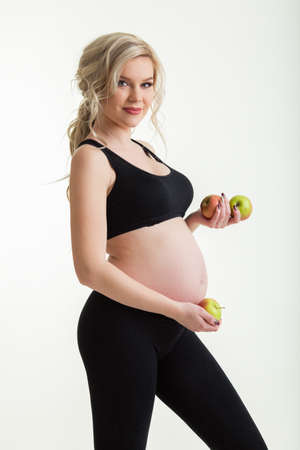 Pregnant sportive beautiful woman with green apples isolated on whiteの写真素材