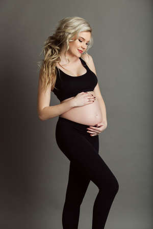 Pregnant beautiful woman is wearing sportive black clothes isolated on gray, healthy life conceptの写真素材