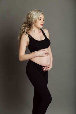 Pregnant beautiful blonde woman is wearing sportive black clothes isolated on gray, healthy life conceptの写真素材