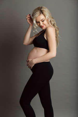Pregnant beautiful blonde woman is wearing sportive black clothes isolated on gray, healthy life conceptの写真素材