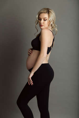 Pregnant beautiful blonde woman is wearing sportive black clothes isolated on gray, healthy life conceptの写真素材