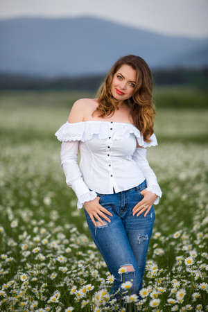 Beautiful girl on the camomile field is wearing casual clothes, spring timeの写真素材