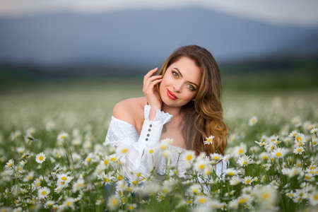 Beautiful woman on the camomile field is wearing white dress, spring timeの写真素材