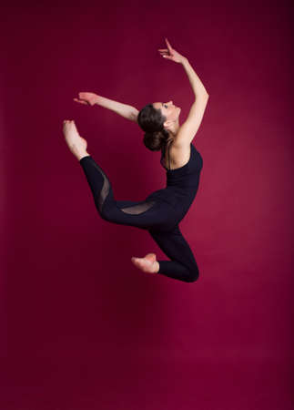 Beautiful slim flexible woman is wearing black body costume in studio isolated on redの写真素材