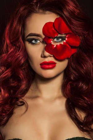 Portrait of beautiful sexy woman with creative makeup and red rose petals of her faceの写真素材