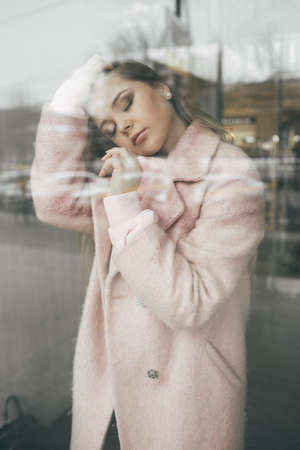 Unhappy pretty blonde girl behind the window, spring time