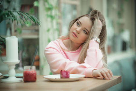 Pretty blonde girl with long hair is sitting on veranda in cafe and having breakfastの写真素材