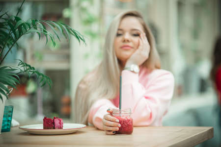 Cute blonde girl is sitting on veranda in cafe and having nice breakfast