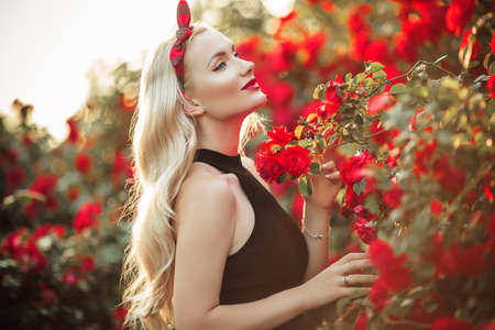 Portrait of beautiful happy blonde girl in bush of red rosesの写真素材