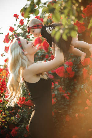 Beautiful blonde woman with little baby girl in bush of red rosesの写真素材