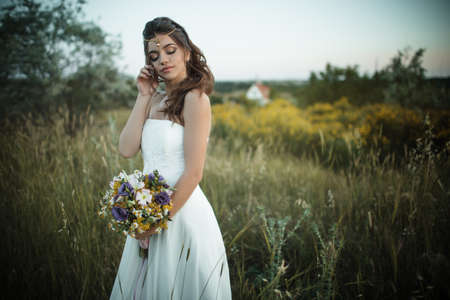 Beautiful young bride is wearing teak with fashion bouquet of wildflowers in yellow field, nature wedding conceptの写真素材