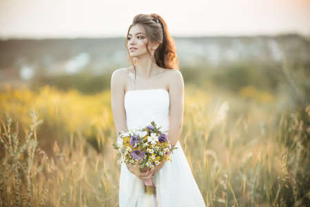 Beautiful young bride is holding fashion bouquet of wildflowers in yellow field, nature wedding conceptの写真素材