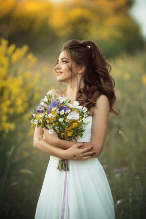 Beautiful lovely bride is wearing white fashion dress holding bouquet of wildflowers in yellow field, nature wedding conceptの写真素材