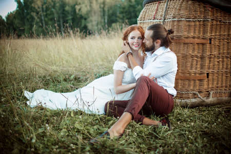 Happy wedding couple are sitting near airballoon basket in the sunny field.の写真素材
