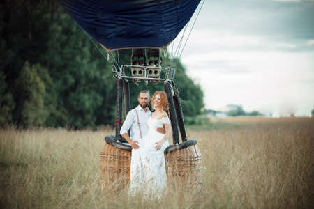 Happy wedding couple are sitting inside airballoon basket in the sunny field.の写真素材