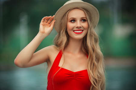 Pretty smiling teen girl is wearing red swimsuit and hat resting near swimming pool with blue water. summer vacationsの写真素材