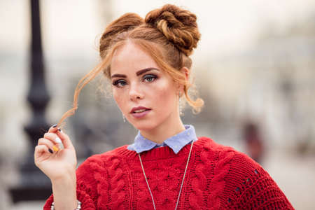 Pretty smiling curly redhaired girl is wearing red knitted sweater walking on the street, autumn timeの写真素材
