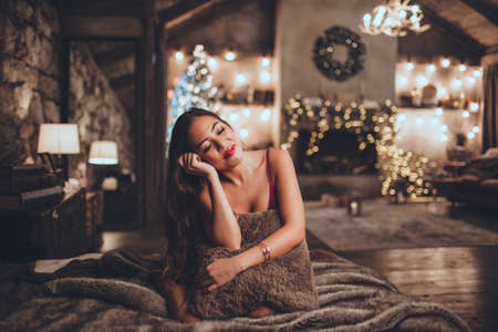 Beautiful asian woman is sitting at home near christmas tree in cozy interior. Interior with christmas decorations.の写真素材
