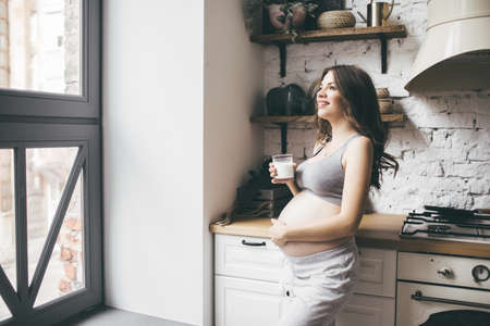 Pretty pregnant woman in kitchen with cup of milk