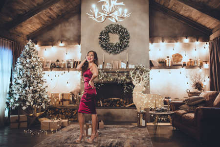 Young beautiful asian girl is fashion red dress sitting at home near christmas tree in cozy interior. Interior with christmas decorations.の写真素材