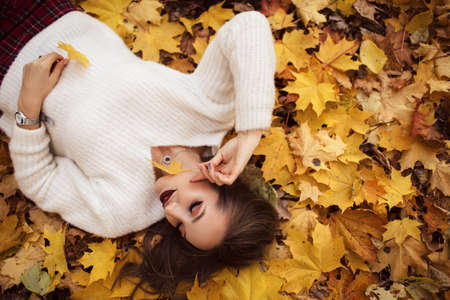 Pretty stylish woman with fashion makeup is lying down on carpet of yellow maple leavesの写真素材