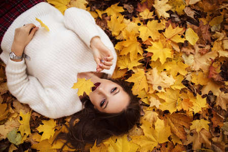 Pretty stylish woman with fashion makeup is lying down on carpet of yellow maple leavesの写真素材