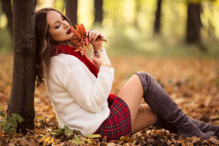 Pretty woman is wearing fashion clothes sitting in autumn parkの写真素材