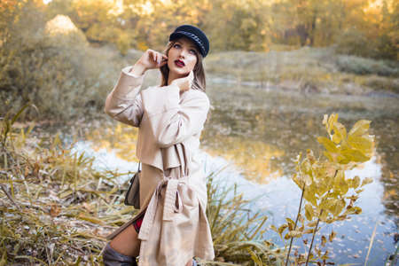 Pretty stylish woman with fashion makeup in autumn park is wearing hat and coatの写真素材