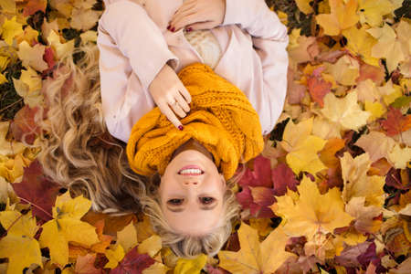 Pretty blonde girl is lying in park on the carpet of yellow maple leavesの写真素材