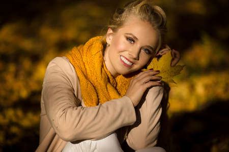 Pretty smiling blonde girl in yellow autumn leavesの写真素材