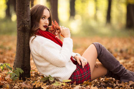 Pretty woman is wearing fashion clothes sitting in autumn parkの写真素材