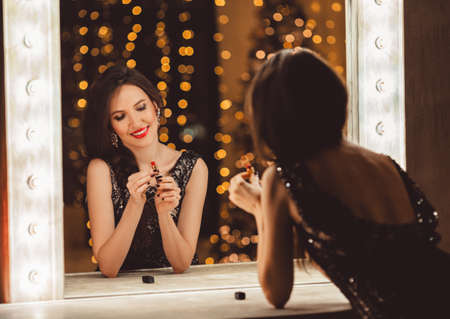 Beautiful young woman is wearing luxury dress infront of mirror with red lipstickの写真素材