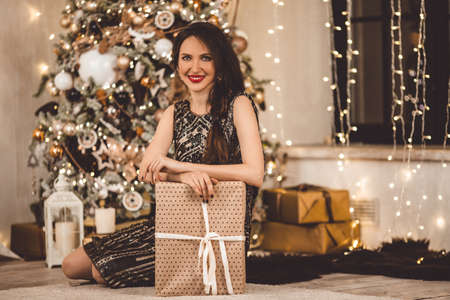 Beautiful young woman is wearing luxury dress against the background of a Christmas tree with gift boxの写真素材
