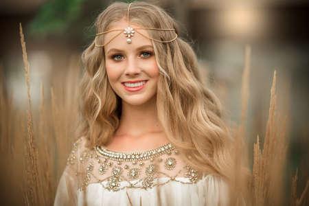 Portrait of happy smiling blonde girl with long blonde hair is wearing white fashion dress in field of rayの写真素材