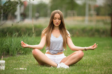 Young sportive girl doing yoga meditation in park in the cityの写真素材