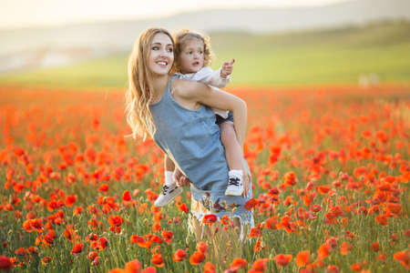 Beautiful smiling child girl with mother are having fun in field of red poppy flowers over sunset lights, spring timeの写真素材