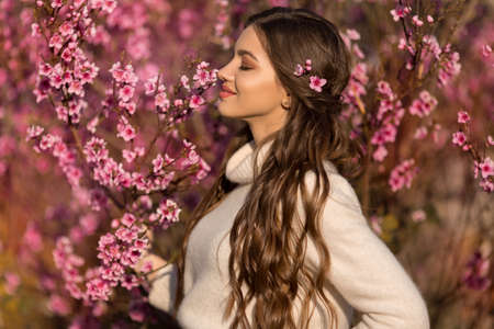 Young beautiful teen girl with perfect skin and makeup is wearing romantic clothes posing near blossom tree in cherry gardenの写真素材
