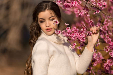Young beautiful teen girl with perfect skin and makeup is wearing romantic clothes posing near blossom tree in cherry gardenの写真素材