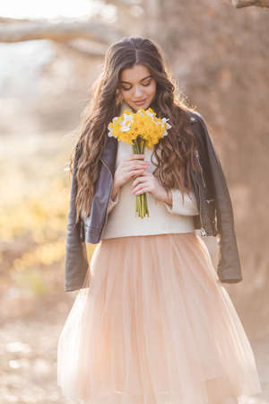 Pretty smiling teenager girl are holding bouquet of narcissus flowers in park over sunset lights. Spring timeの写真素材