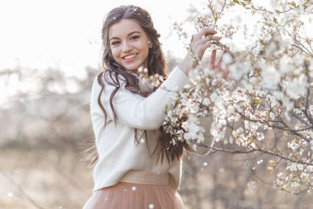 Pretty smiling teen girl are posing in garden near blossom cherry tree with white flowers. Spring timeの写真素材