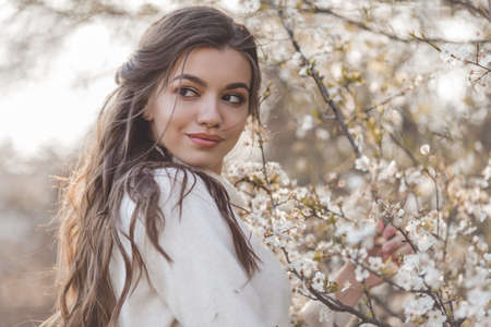 Pretty smiling teen girl posing near blossom cherry tree with white flowers.の写真素材